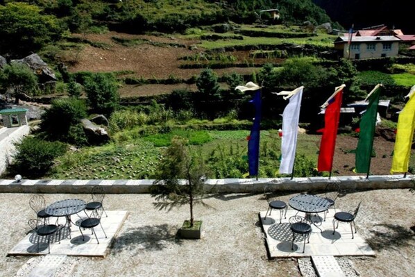 A terrace with outdoor seating and a view of terraced fields and a house in the background. - Mountain Lodges of Nepal - Monjo (Monjo)