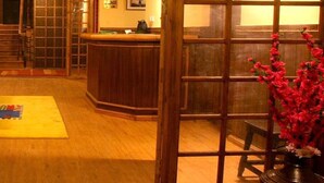 A reception area with a wooden reception desk, a yellow mat, and a vase with red flowers.