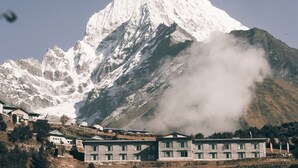 A mountain with a snow-capped peak and a building with multiple windows in the foreground. - Mountain Lodges of Nepal - Namche (Namche Bazar)