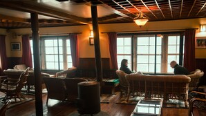 A cozy room with wicker furniture, a wood-burning stove, and large windows with red curtains. - Mountain Lodges of Nepal - Namche (Namche Bazar)