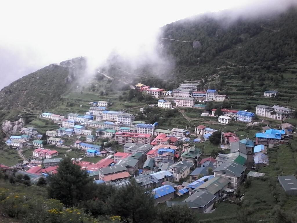 A hillside village with colorful buildings, terraced fields, and a mountainous backdrop.