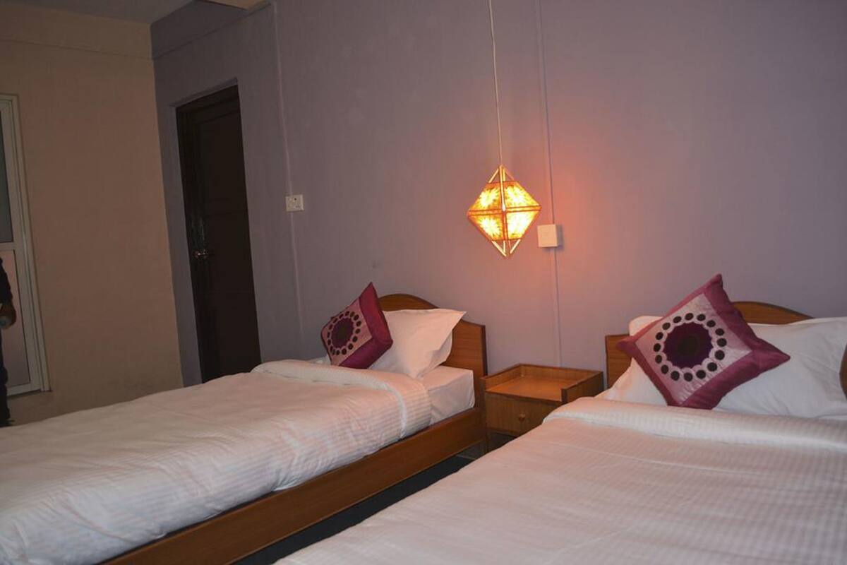 Una habitación de hotel con dos camas individuales, una mesita de noche, una lámpara colgante y una puerta.