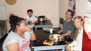 A group of people seated around a table with food and a pot, in a room with a brick wall and a woven ceiling. - Bodhi Guest House (Kathmandu)