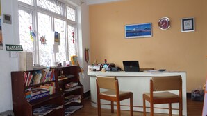 A reception desk with a laptop, two chairs, a bookshelf, and a window with a 'MASSAGE' sign. - Bodhi Guest House (Kathmandu)