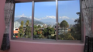 A room with a large window offering a view of a mountain range and a town below.