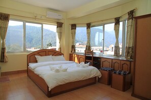 A hotel room with a large bed, a desk, and a view of mountains. - Hotel Milarepa (Pokhara)