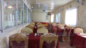 A banquet hall with tables covered in red tablecloths, chairs with bow decorations, and large windows.
