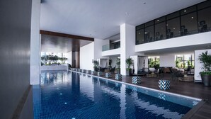 Ein moderner, überdachter Pool mit Fliesenboden, umgeben von Entspannungsbereichen mit Sitzgelegenheiten und Pflanzen in Töpfen.