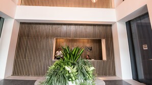 Eine moderne Lobby mit Holzboden, einer Rezeption und einem runden Tisch mit Pflanzen.