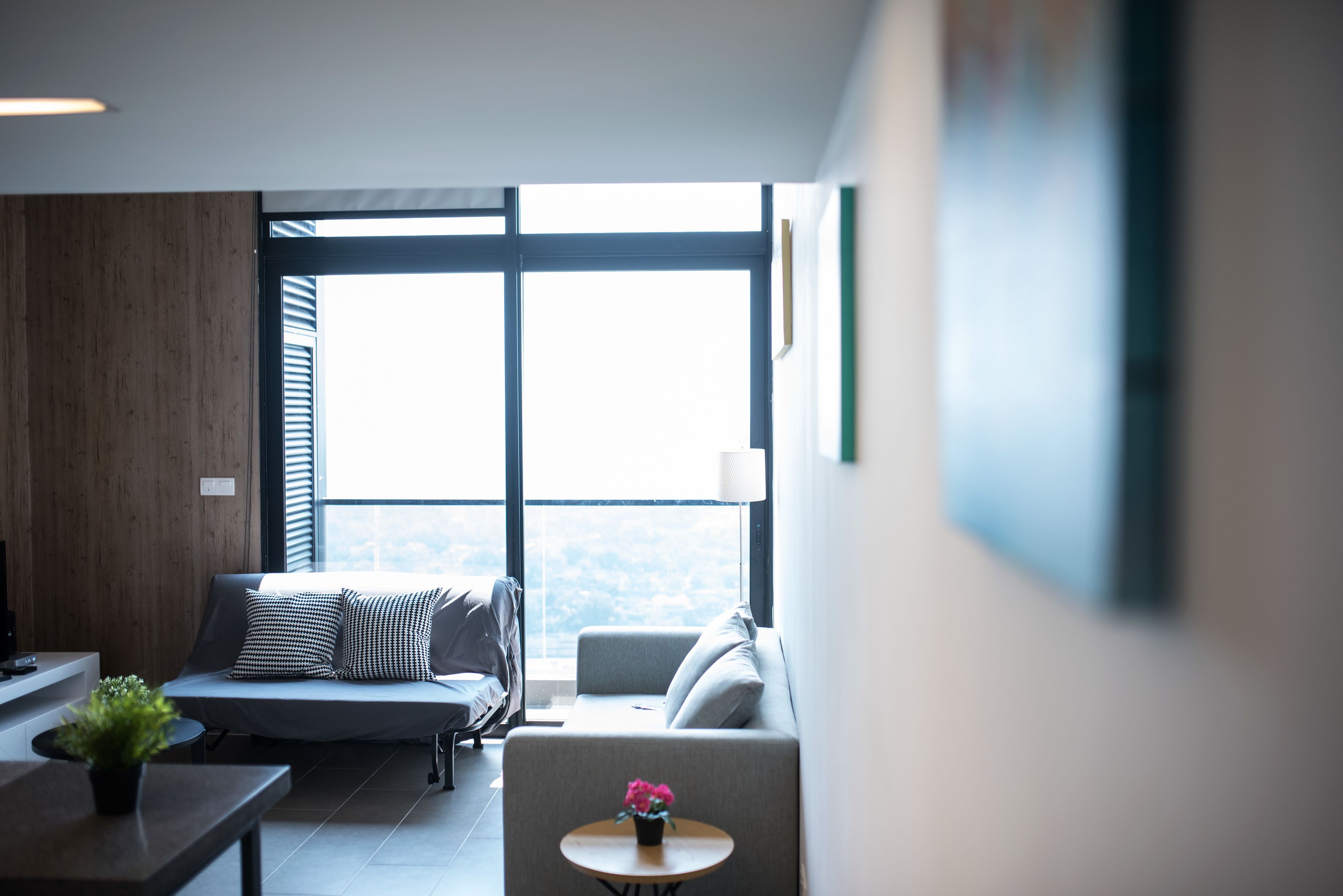 A modern living room with a sofa, a small table with a plant, and a view through large windows.