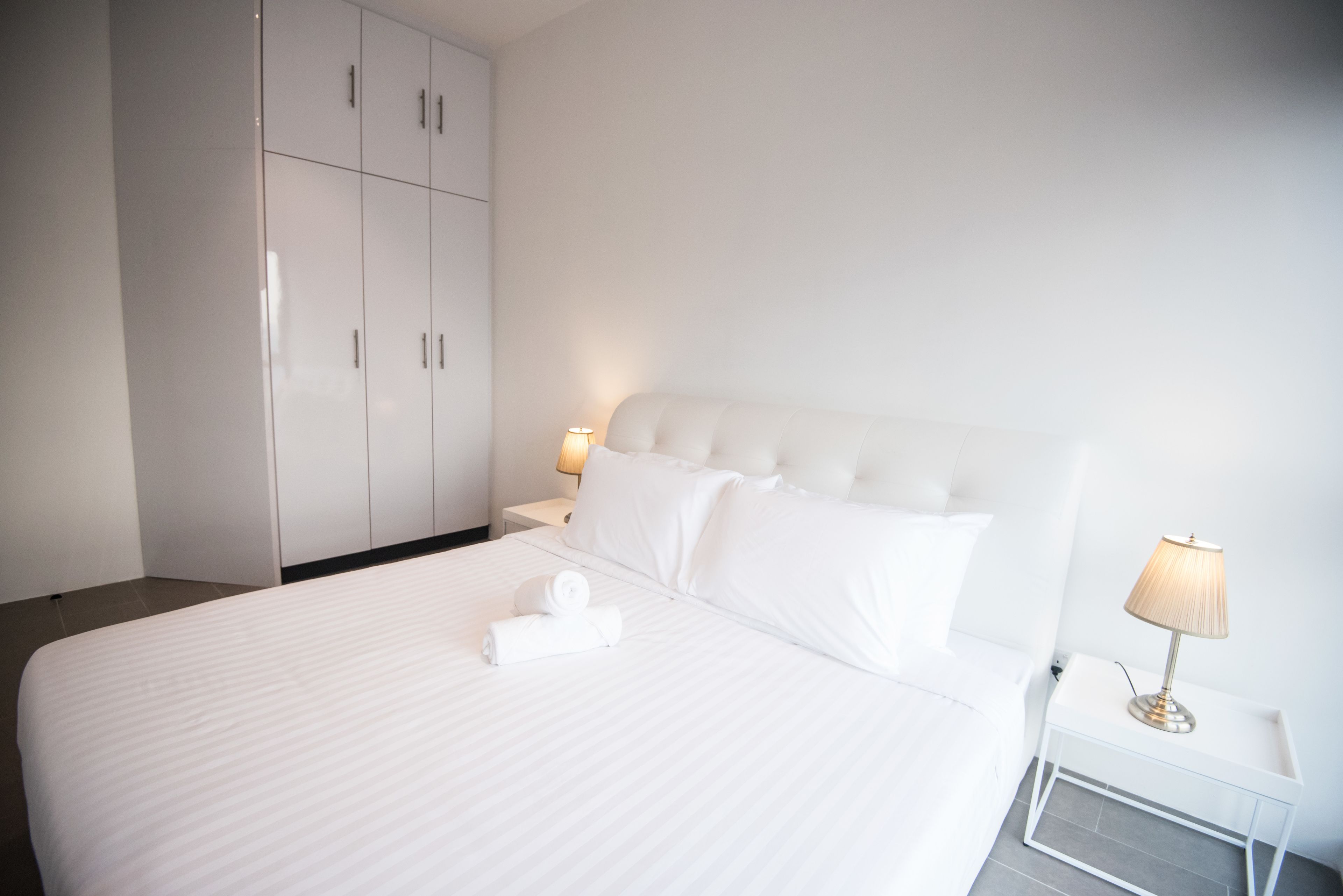 Une chambre d’hôtel avec un grand lit, du linge de lit blanc, une table de chevet avec une lampe et une armoire.