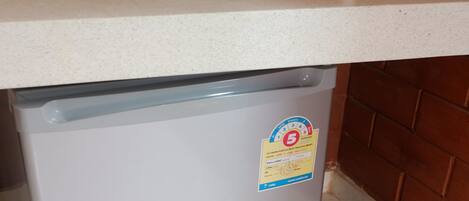 Un petit réfrigérateur placé sous un plan de travail blanc, avec une prise électrique sur le mur.