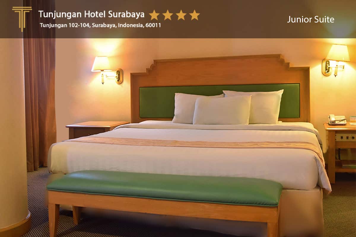 A junior suite with a bed, green headboard, bedside lamps, and a bench.