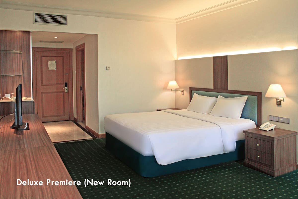 A Deluxe Premiere hotel room with a bed, bedside lamps, a nightstand, a desk, and a television.