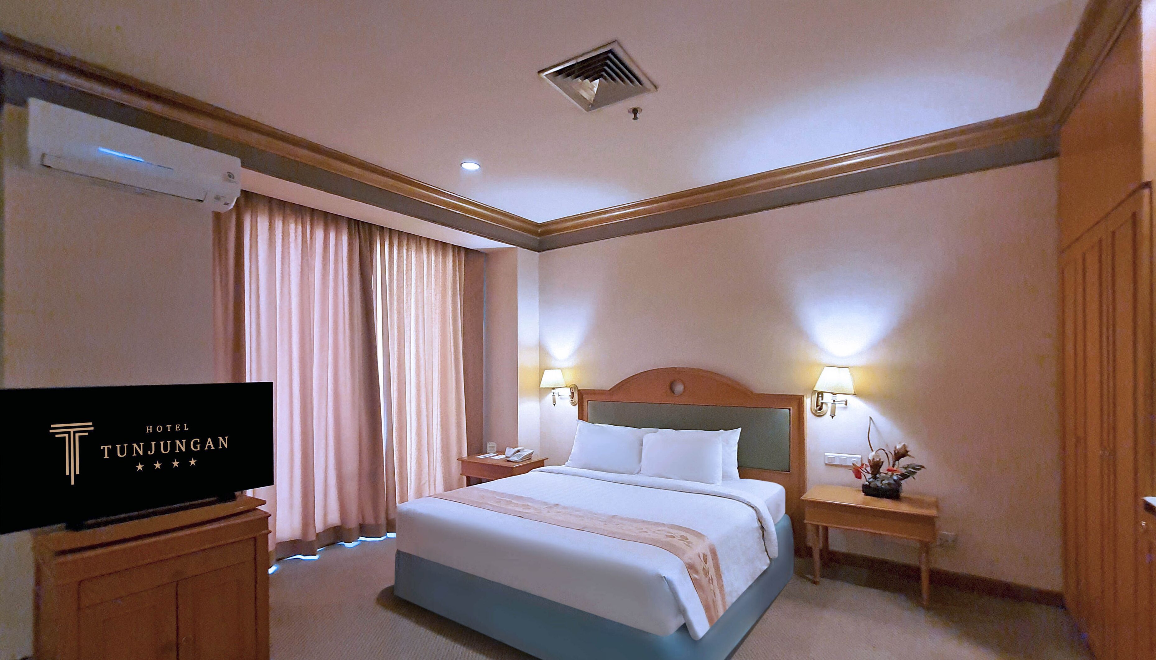 A hotel room with a bed, two bedside lamps, a nightstand, a TV, and a window with curtains.