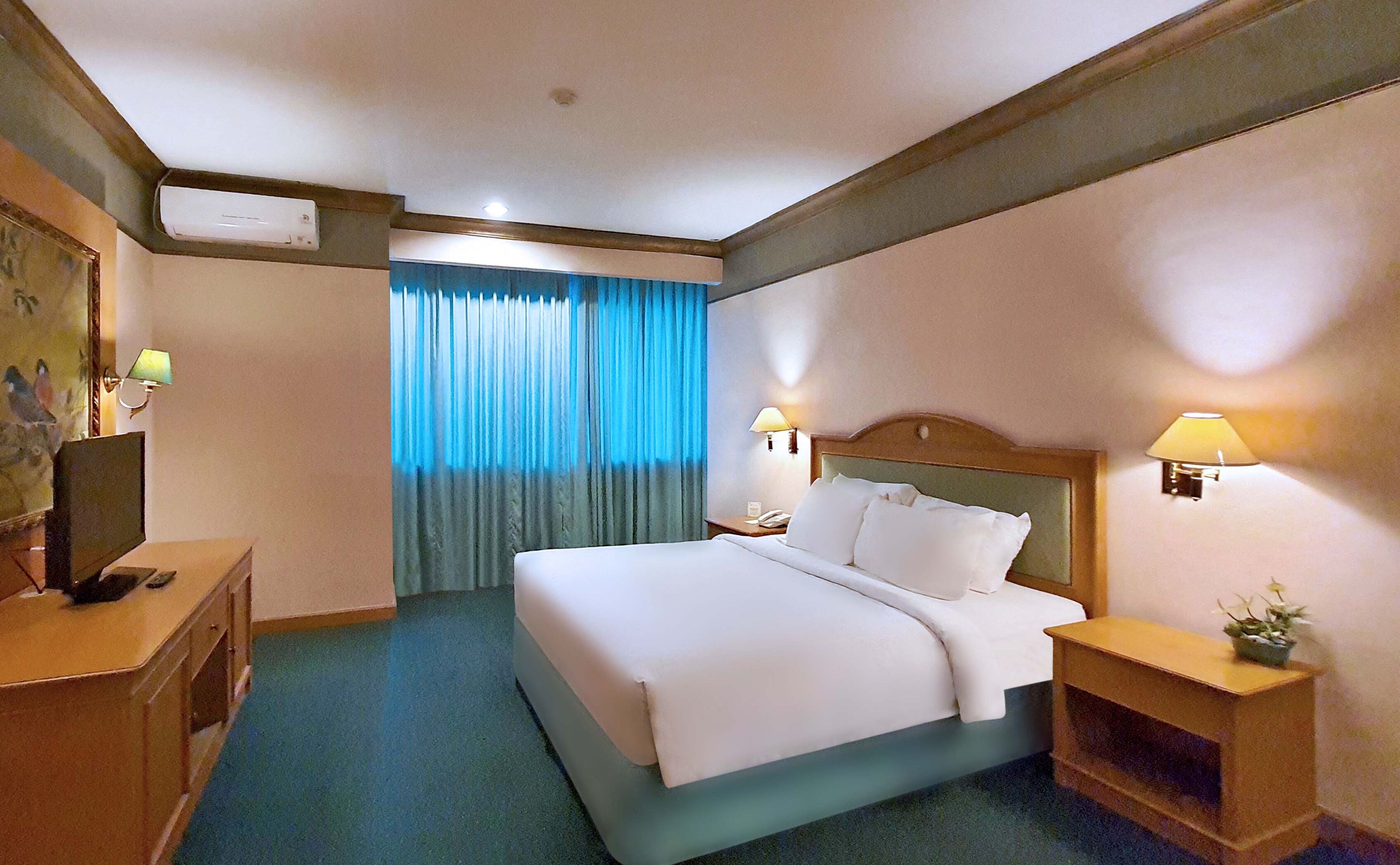 A hotel room with a bed, bedside tables, a desk, and a painting on the wall.