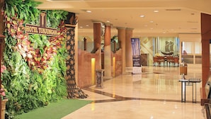 A hotel lobby with a tropical-themed wall, marble flooring, and a ship model display. - Tunjungan Hotel (Surabaya)