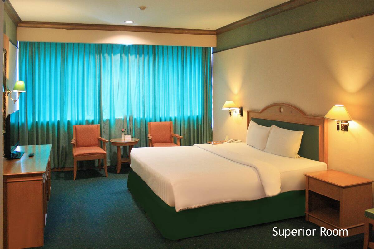 A hotel room with a large bed, two chairs, a small table, and a desk.