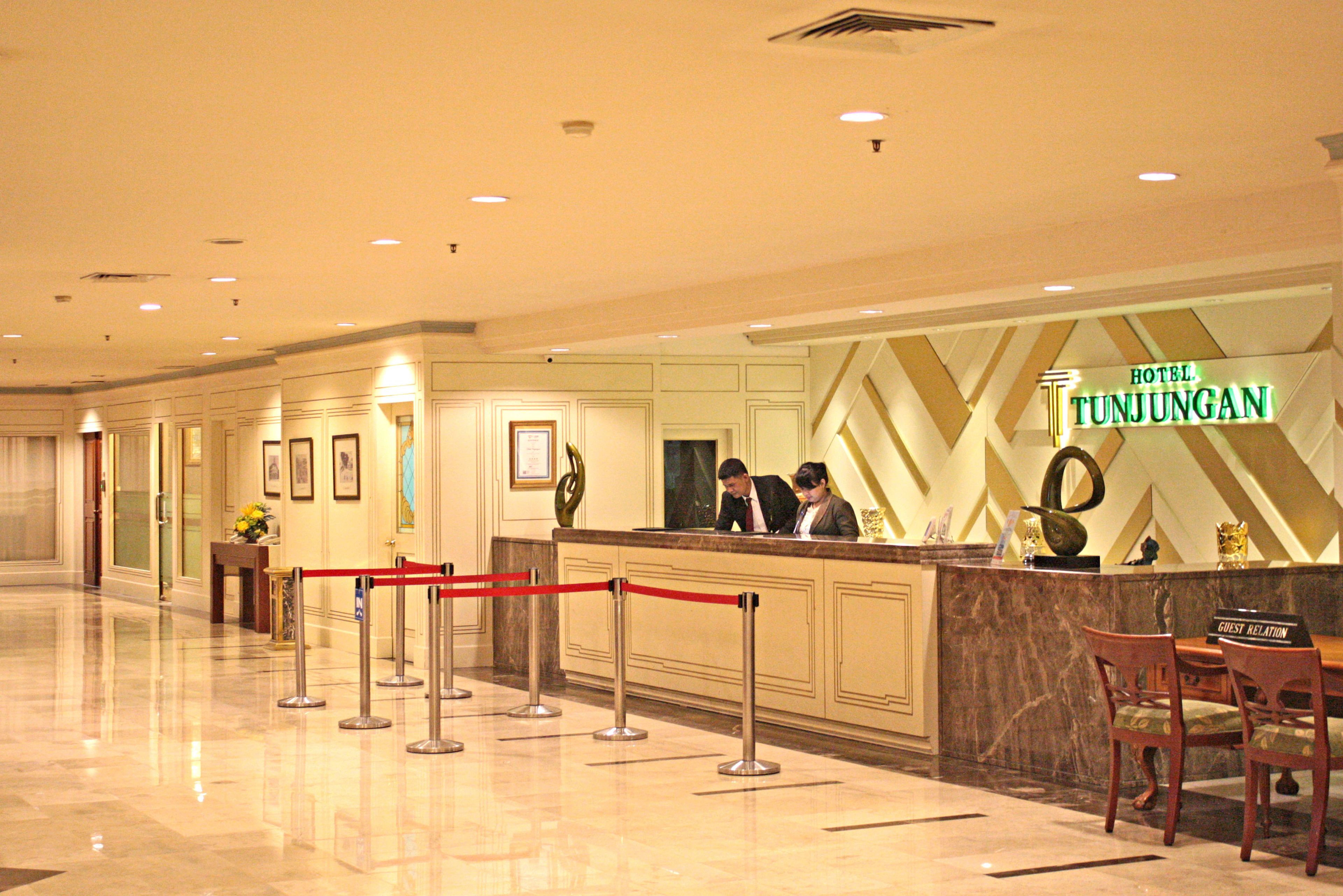 A hotel reception area with a marble counter, red rope barrier, and a sign indicating 'Hotel Tunjungman'.