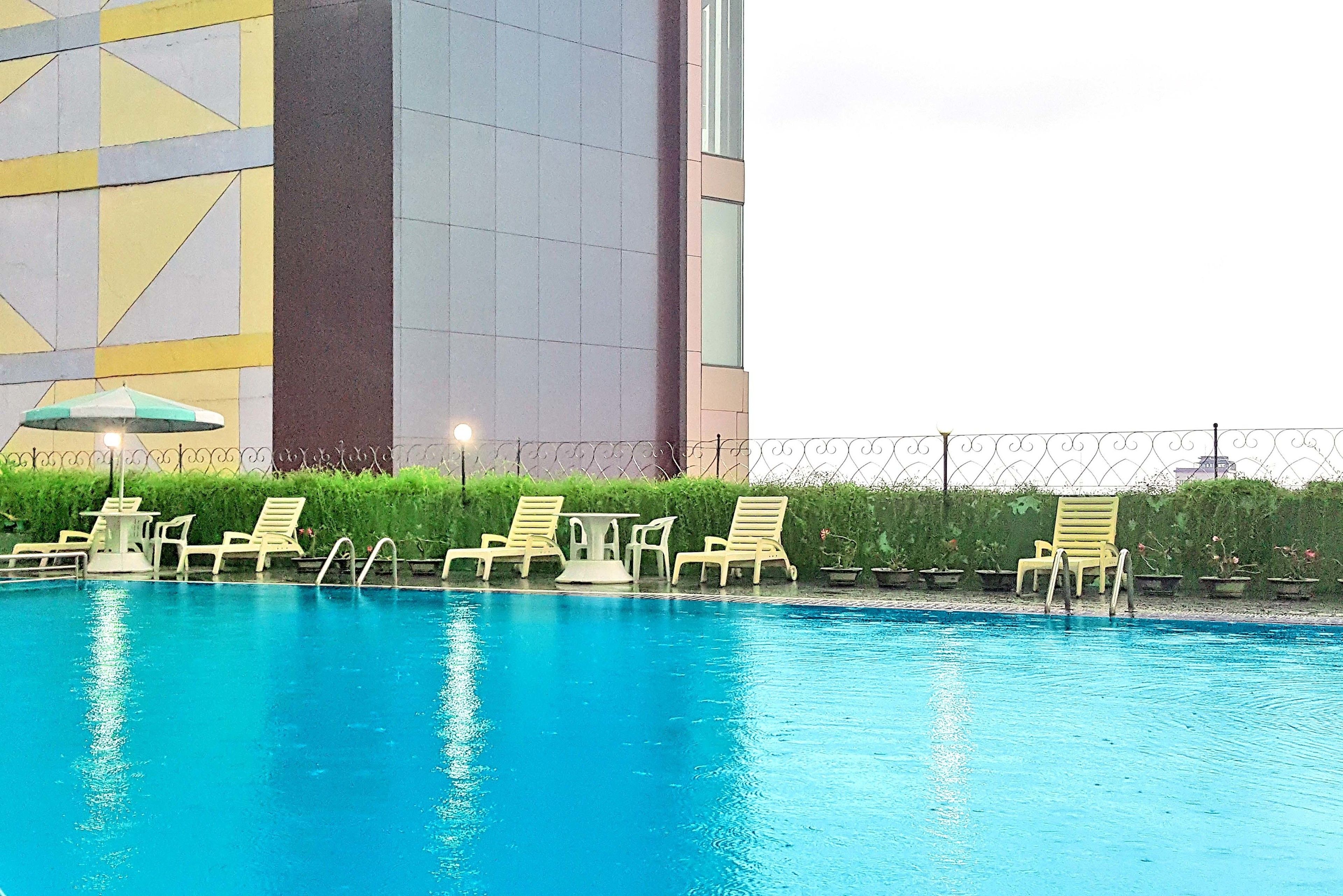 A swimming pool with lounge chairs and a table, surrounded by a fence and greenery.