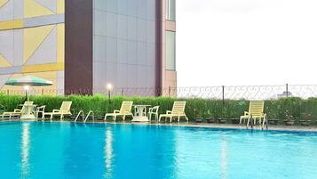 A swimming pool with lounge chairs and a table, surrounded by a fence and greenery.
