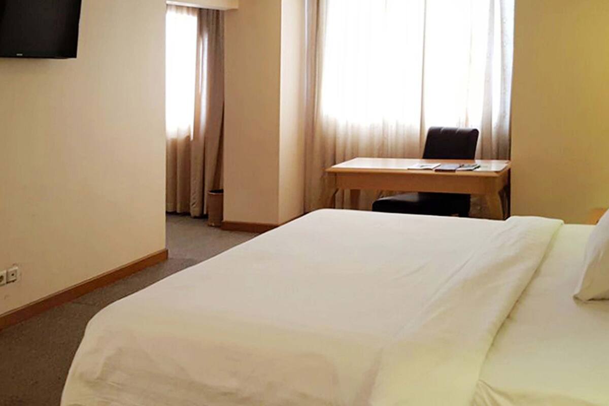 A hotel room with a large bed, a desk, and a chair.