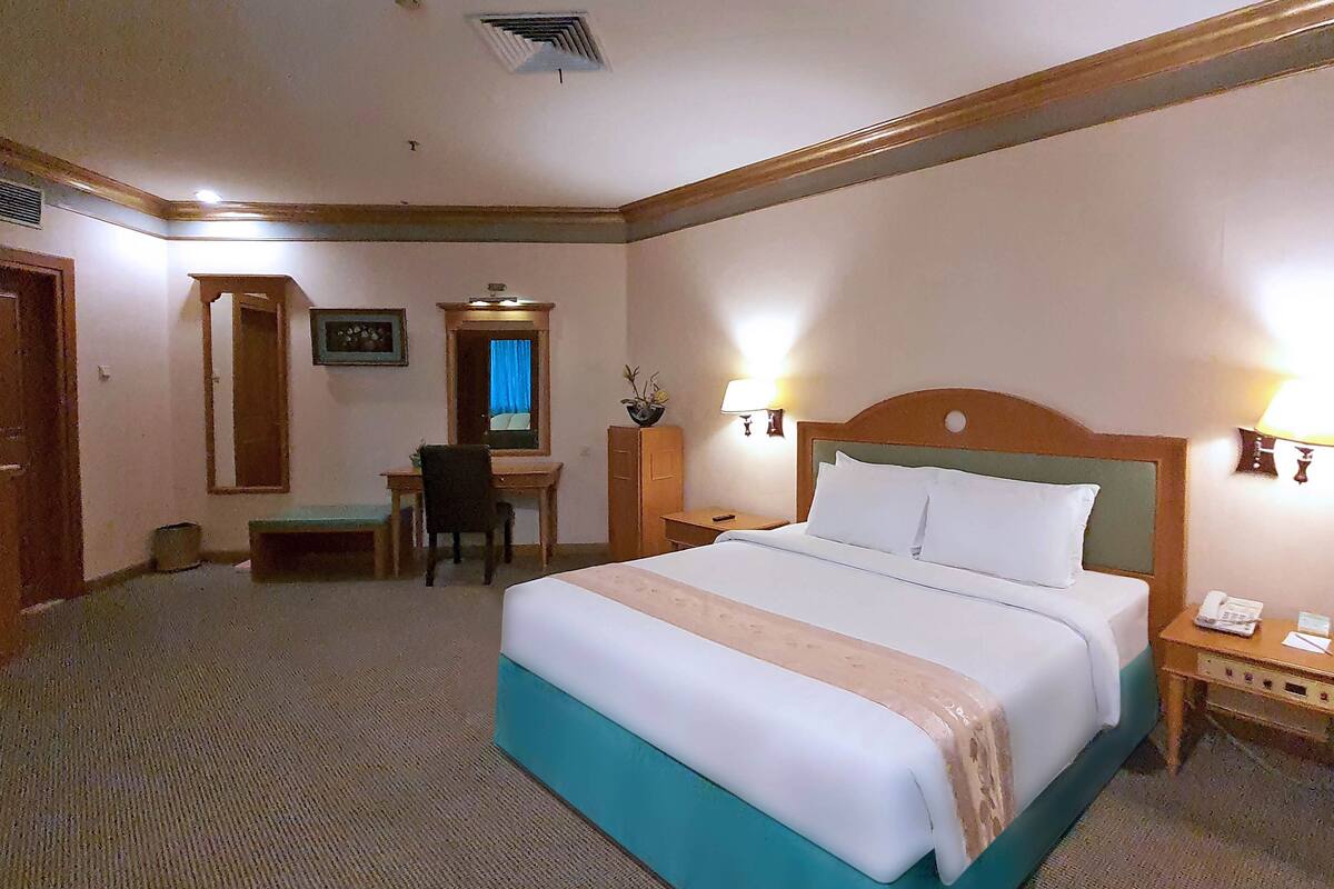 A hotel room with a large bed, a desk, a chair, and two bedside lamps.