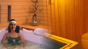 A person in a hot tub with wooden walls and a decorative branch in the background. - Tunjungan Hotel (Surabaya)