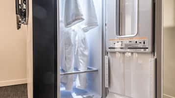 A hotel room with a built-in mini-fridge, a wardrobe, and a small seating area.