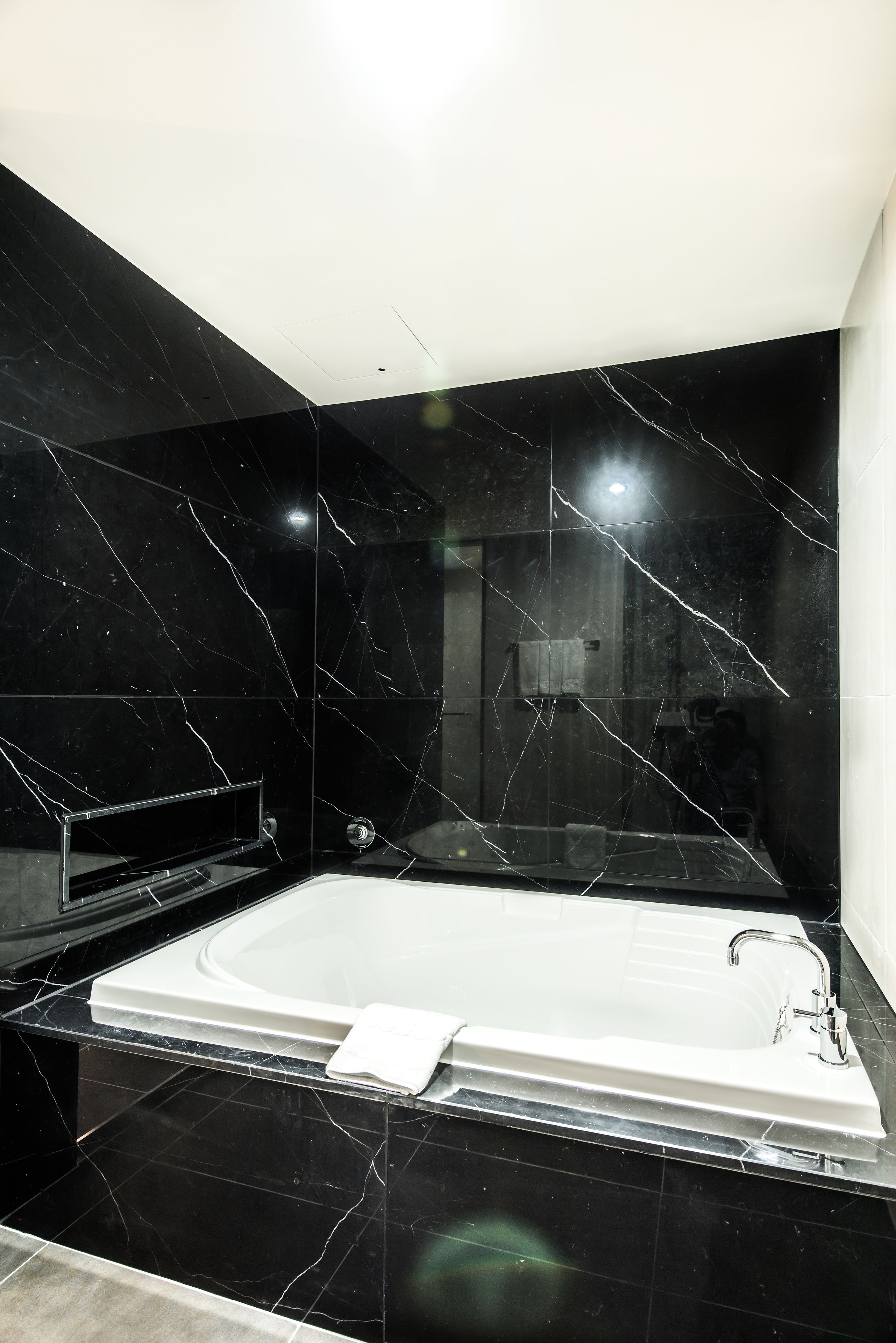 Un baño moderno con una bañera grande, paredes de mármol negro y una zona de ducha visible.