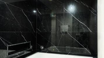 Un baño moderno con una bañera grande, paredes de mármol negro y una zona de ducha visible.