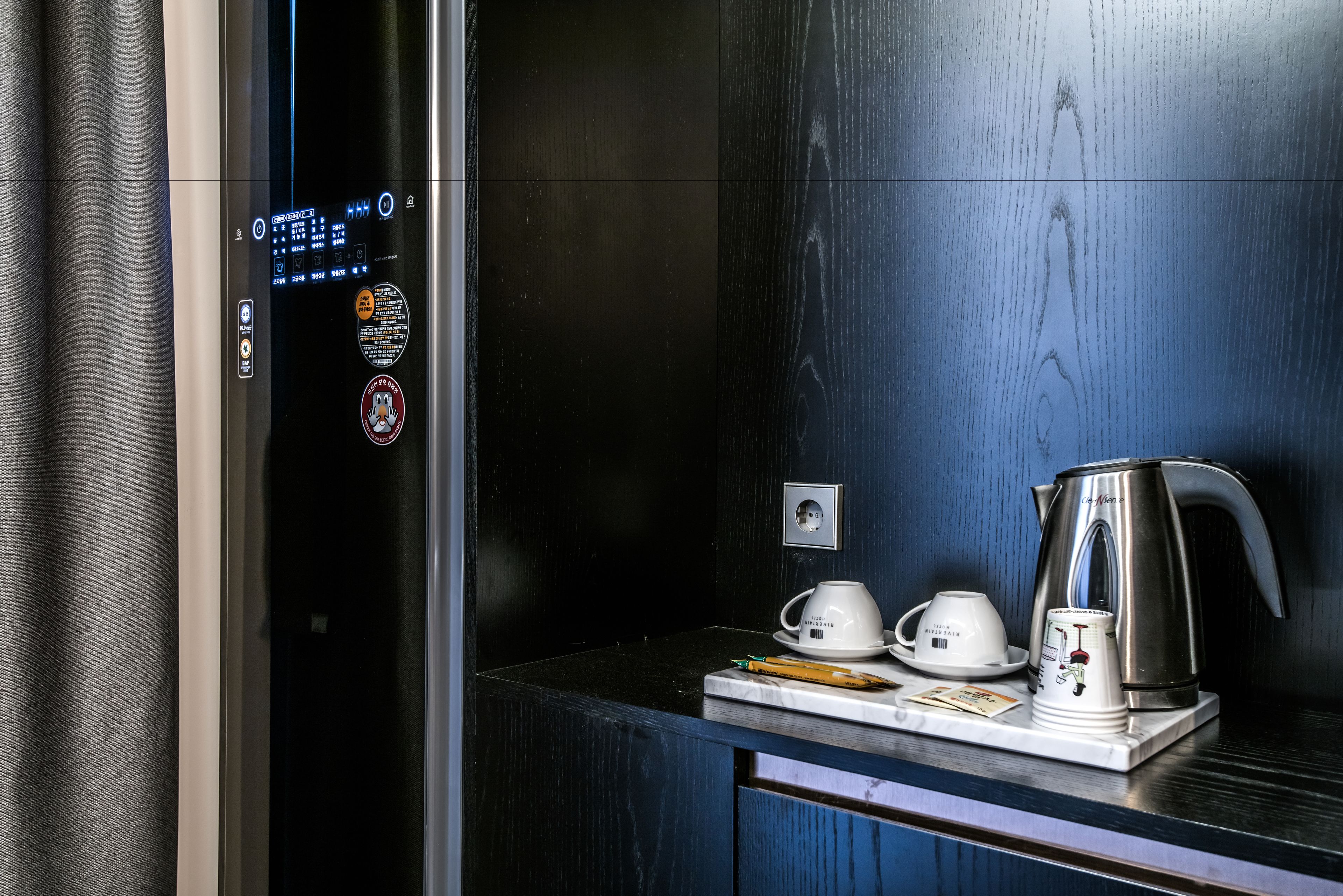 A modern elevator with a digital display, a coffee station with a kettle, cups, and a small table with a notebook and pen.