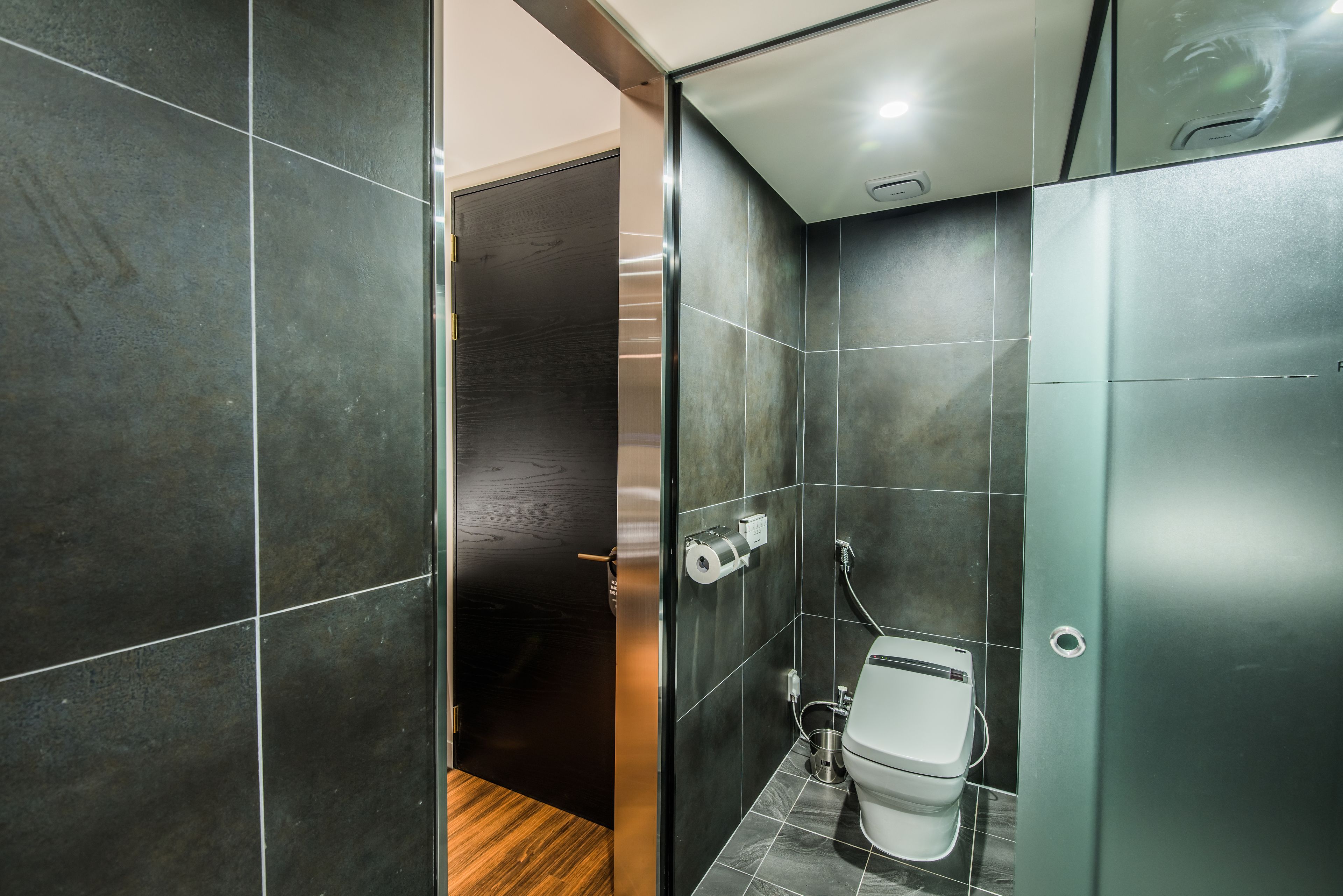 A modern bathroom with dark tiles, a toilet, and a shower area.