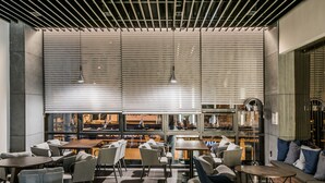 A modern cafe with multiple seating areas, including tables and chairs, and large windows with blinds. - Rivertain Hotel (Daegu)