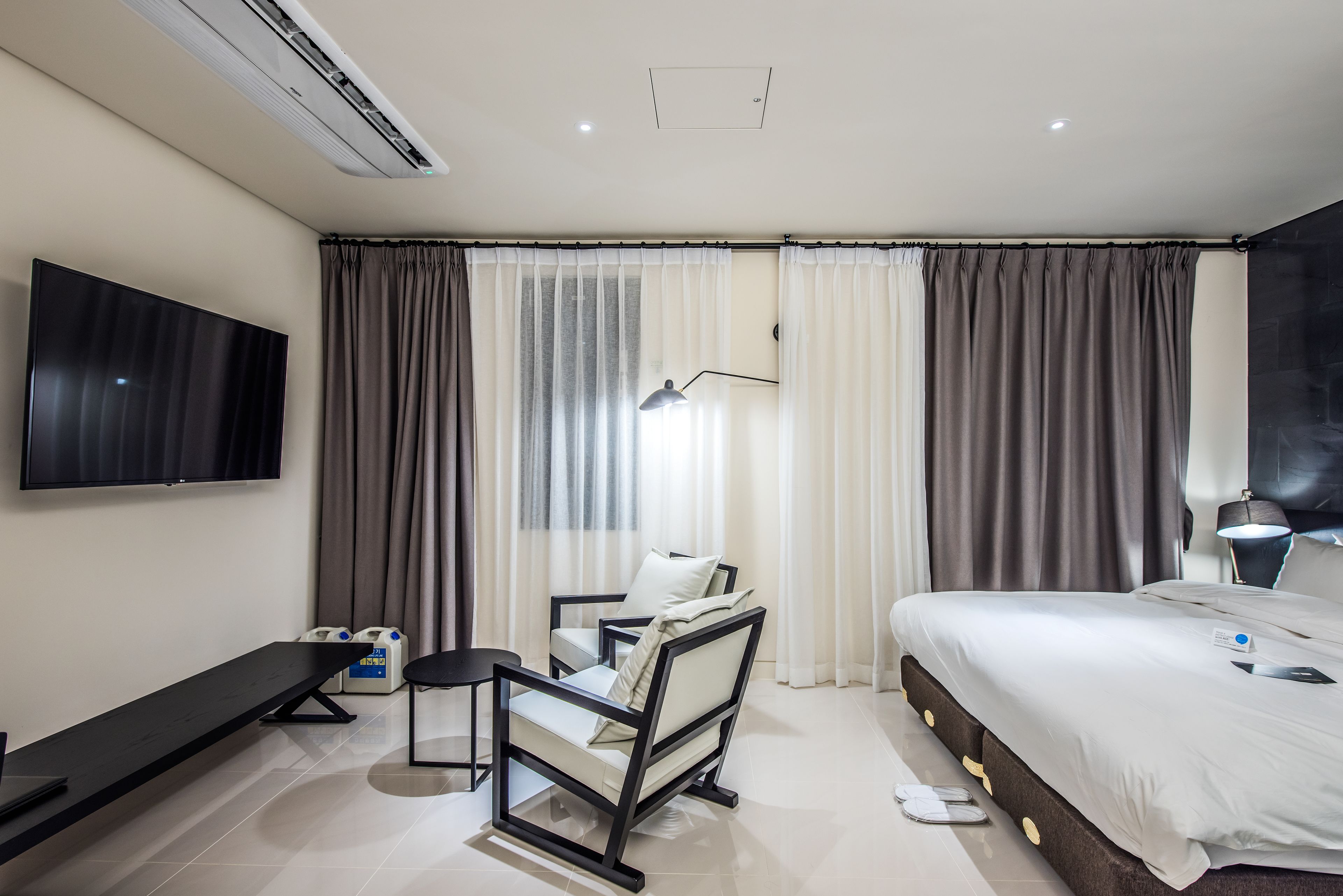 A modern hotel room with a large bed, a desk with a chair, a flat-screen TV, and a window with curtains.