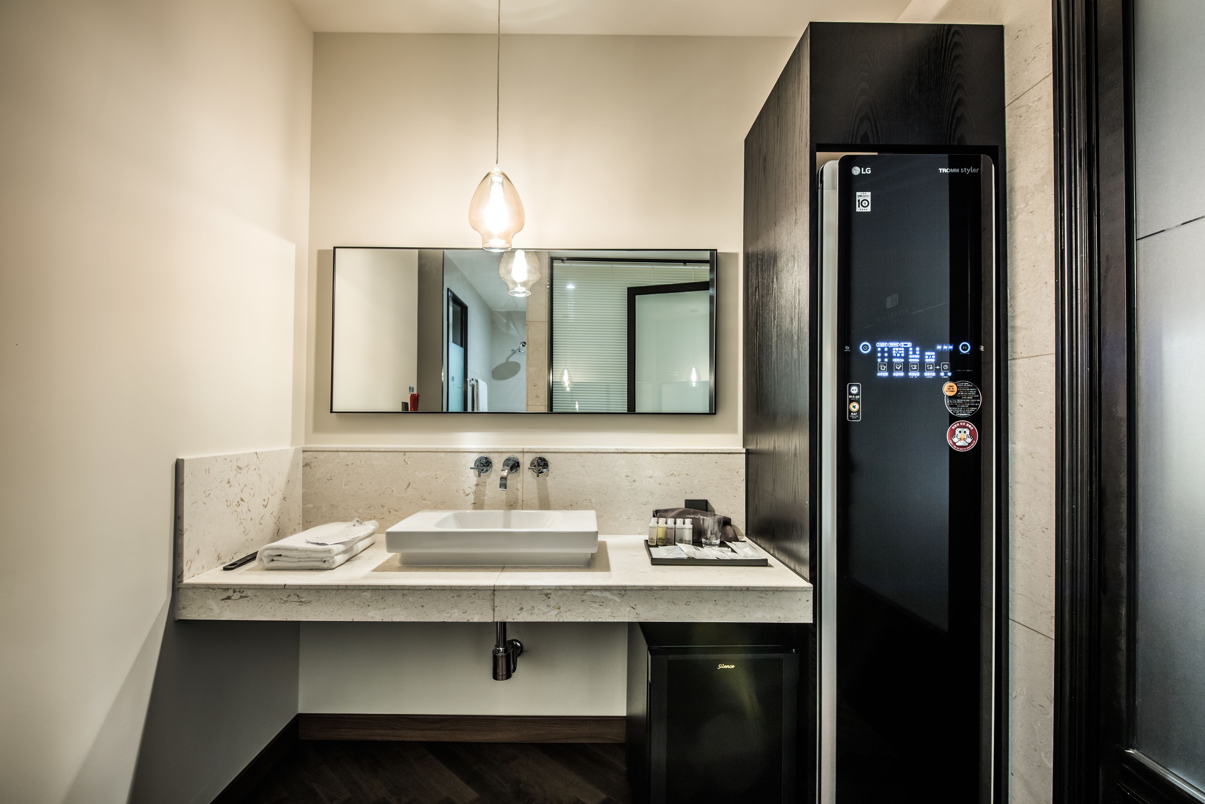 A modern bathroom with a white sink, a mirror, a black refrigerator, and a pendant light.