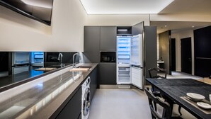 A modern kitchen with a built-in washing machine, a large island, and a dining area with a dark table. - Rivertain Hotel (Daegu)