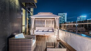 A balcony with a canopy bed, wicker furniture, and a city view at night. - Rivertain Hotel (Daegu)
