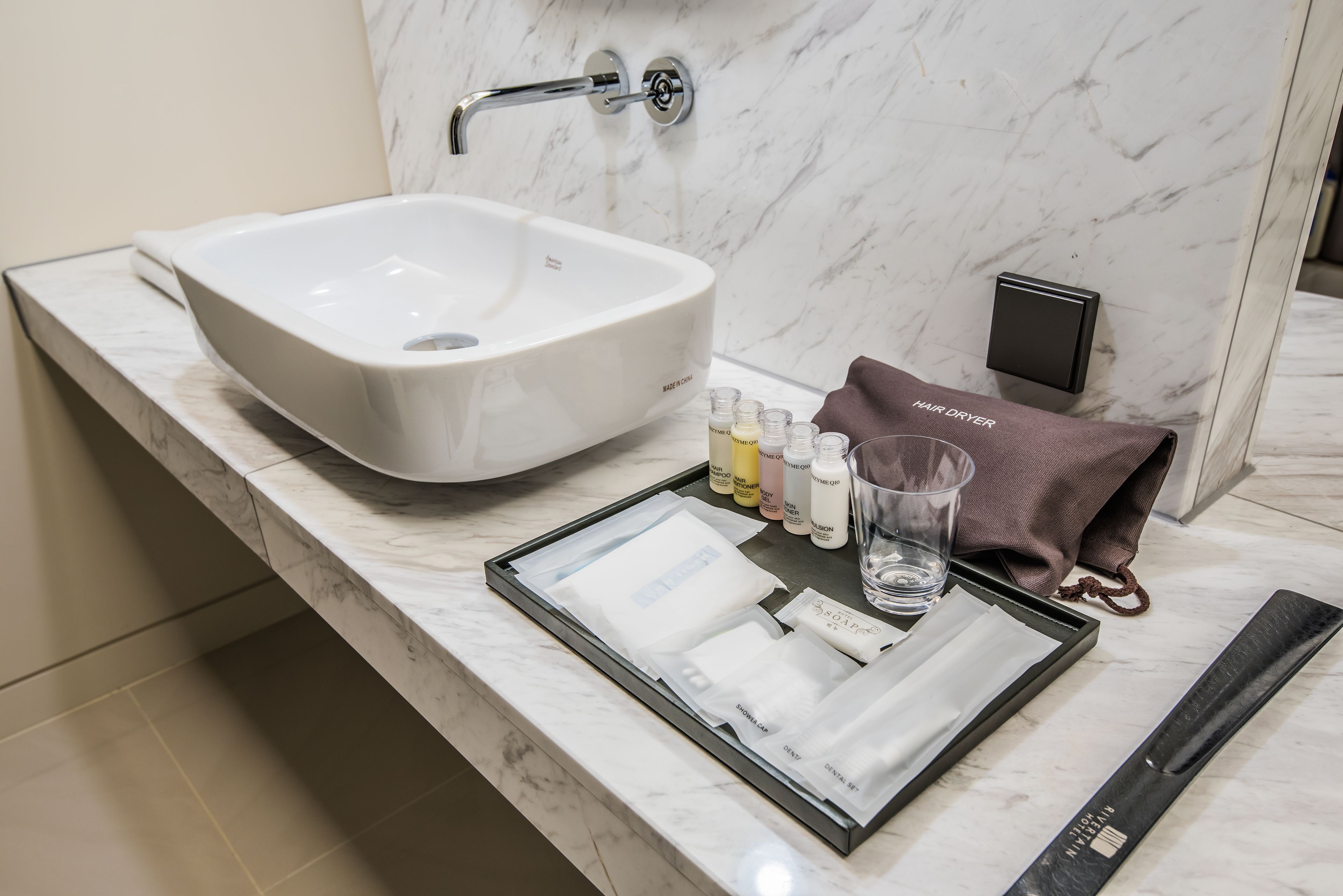A bathroom with a large white sink, a marble countertop, a hair dryer, and toiletries.
