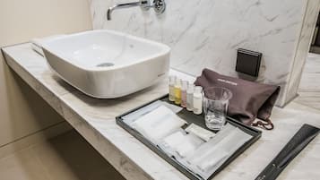 A bathroom with a large white sink, a marble countertop, a hair dryer, and toiletries.