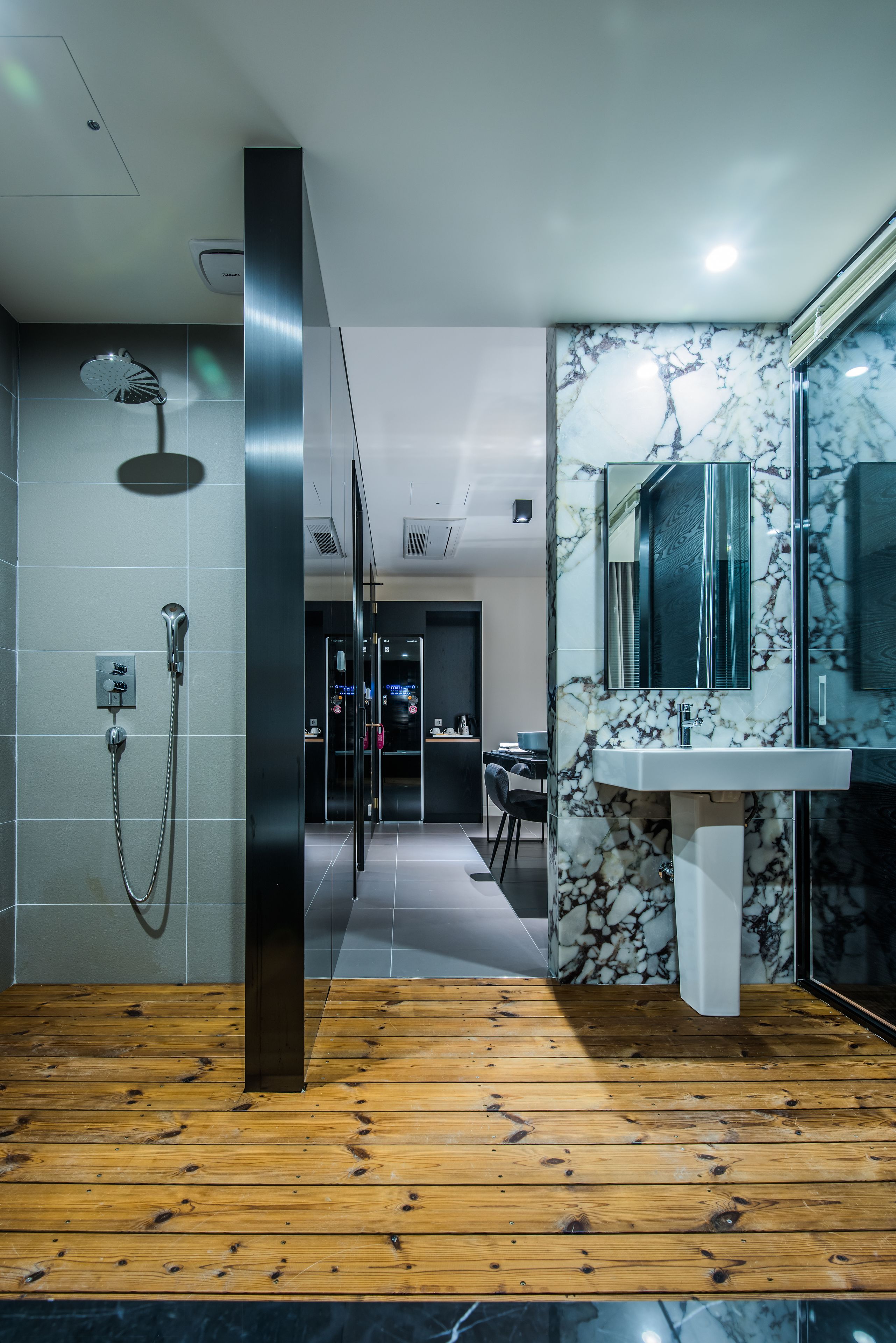 A modern bathroom with a wooden floor, a shower, a marble sink, and a glass-enclosed shower area.