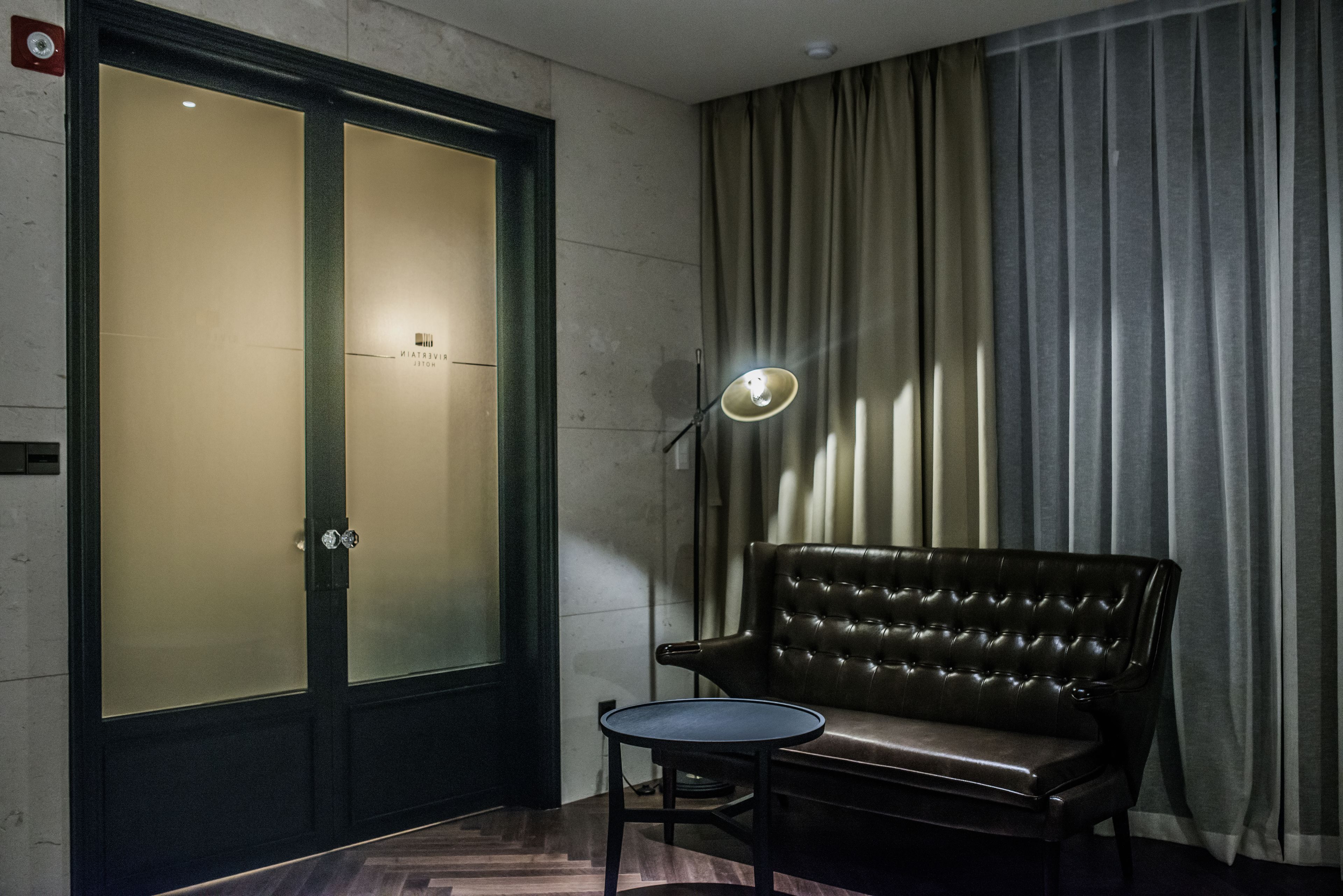 A room with a large frosted glass door, a leather sofa, a small round table, and a floor lamp.
