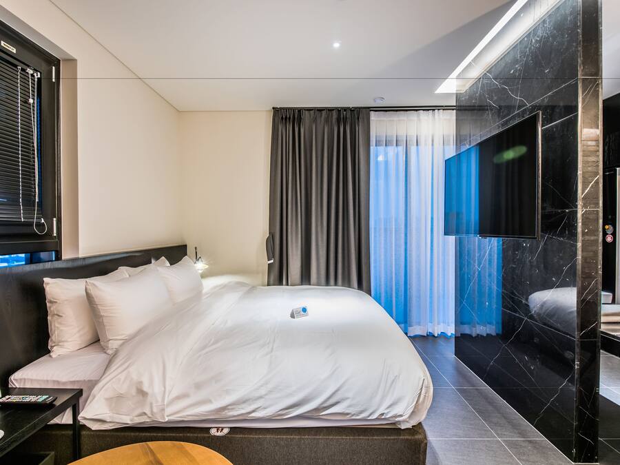 Ein modernes Hotelzimmer mit einem großen Bett, einem Nachttisch mit Telefon, einem Fernseher und Blick auf die Stadt durch das Fenster.