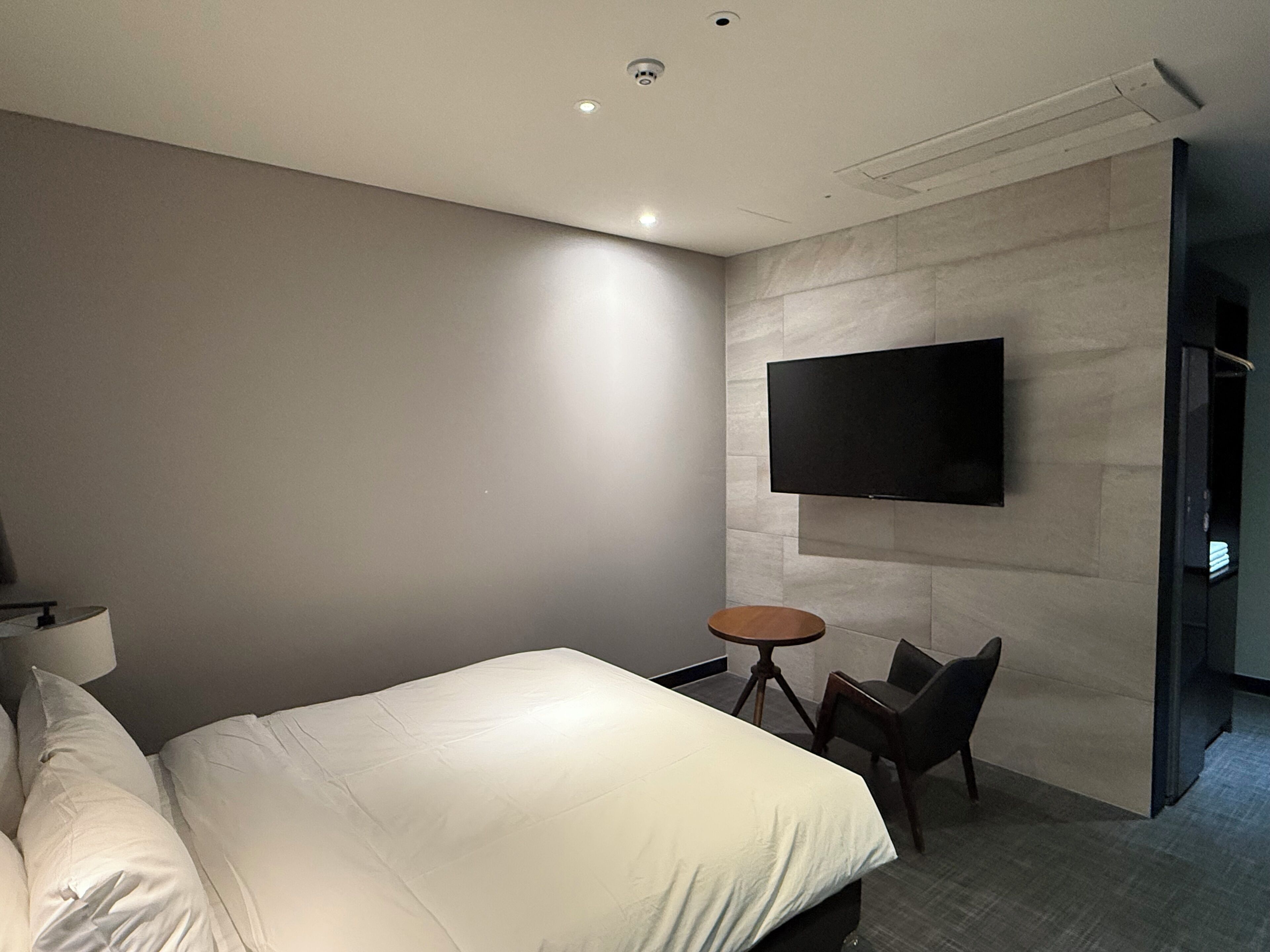 Una habitación de hotel moderna con una cama grande, un televisor de pantalla plana montado en la pared, una pequeña mesa redonda y una silla.