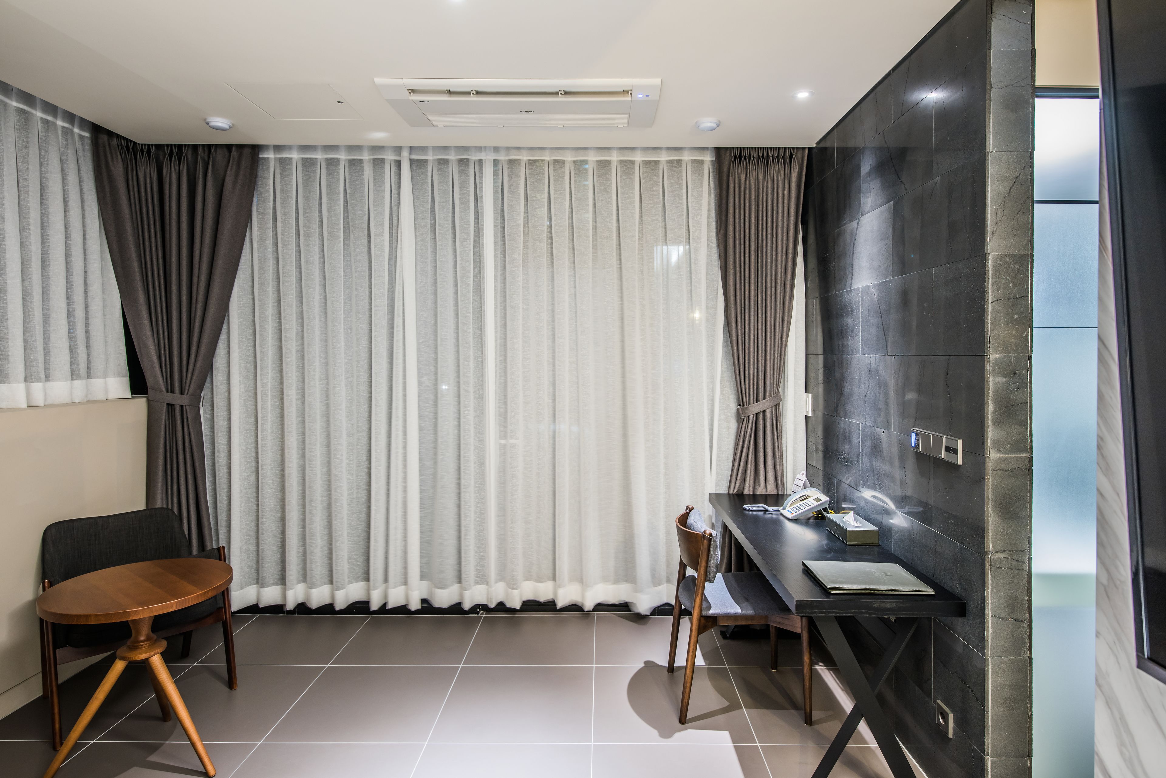 A modern hotel room with a large window, a desk with a chair, and a dark accent wall.