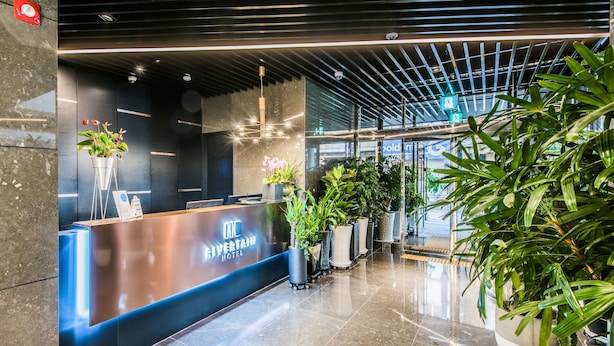 A modern hotel reception area with a reception desk, potted plants, and a polished marble floor. - Rivertain Hotel (Daegu)