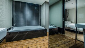 A modern bathroom with a large bathtub, a wooden floor, and a glass shower enclosure. - Rivertain Hotel (Daegu)