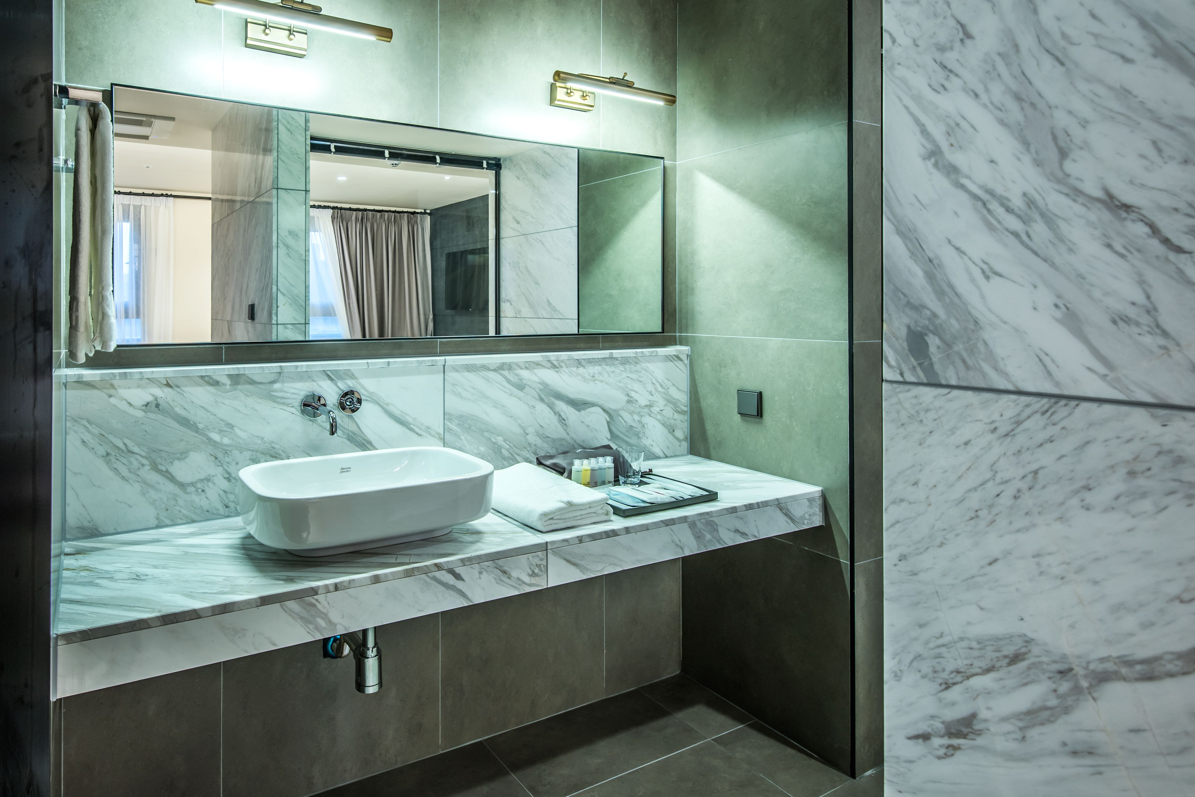 A modern bathroom with a large mirror, a white vessel sink, and a marble countertop.