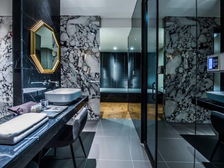 Ein modernes Badezimmer mit Marmorfliesenspiegel, einem großen Spiegel und einer Badewanne.