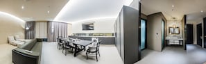 Una habitación de hotel moderna con comedor, sala de estar con sofá y televisor, cocina con mesa y baño con espejo y lavamanos.